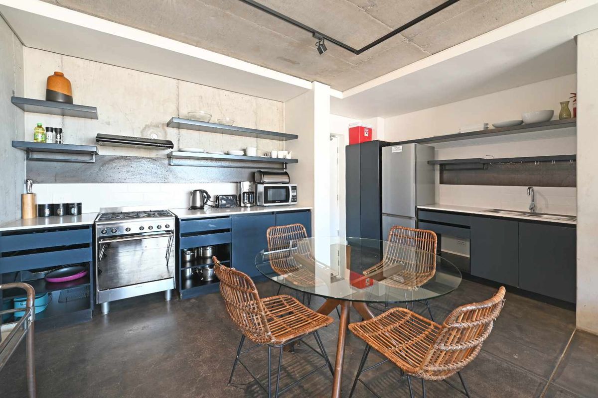 Modern open-plan kitchen and dining area featuring industrial-style exposed concrete ceilings, walls, and polished concrete flooring with sleek dark cabinetry.