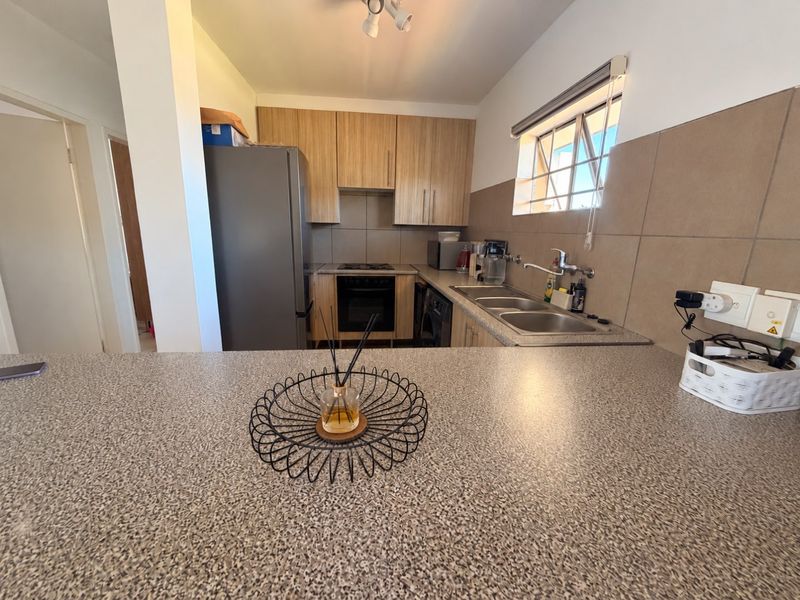 Functional kitchen featuring light wood-tone cabinetry, a double basin sink, built-in oven, and a spacious breakfast bar with durable laminate countertops.