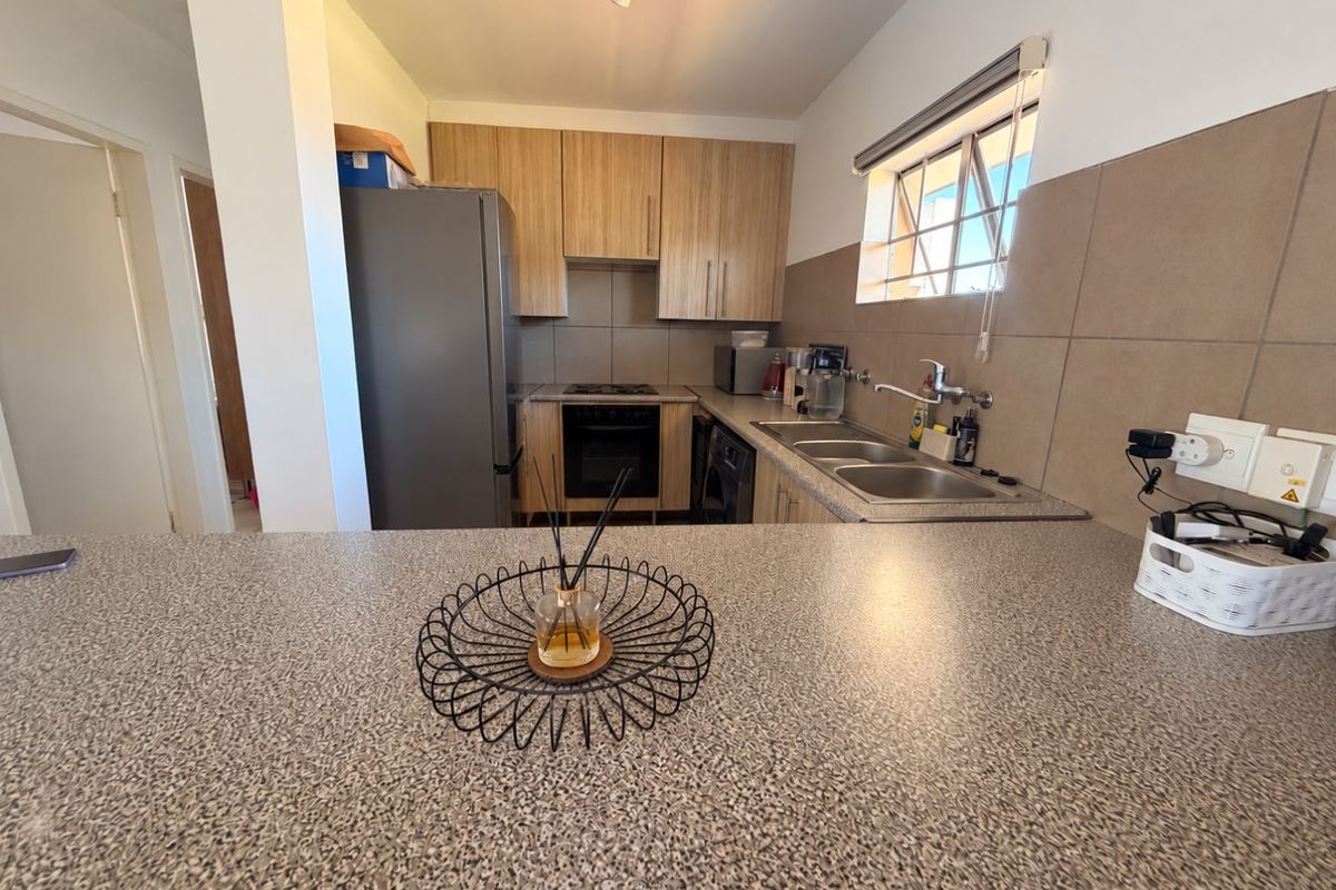 Functional kitchen featuring light wood-tone cabinetry, a double basin sink, built-in oven, and a spacious breakfast bar with durable laminate countertops.