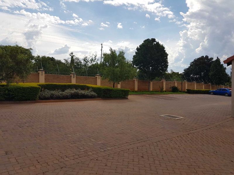 A paved driveway area featuring a perimeter wall with electric fencing and established garden hedges.