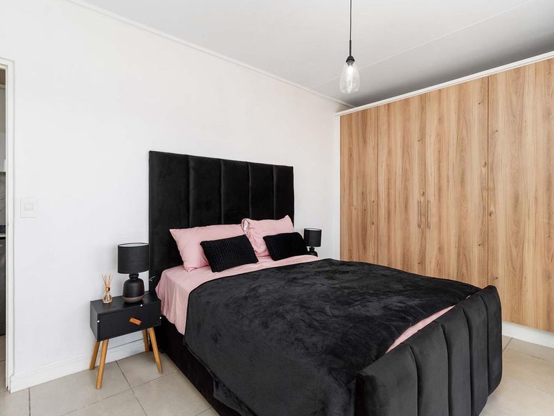 A well-maintained bedroom featuring modern built-in wooden cupboards, neutral tiled flooring, and a contemporary pendant light fixture.