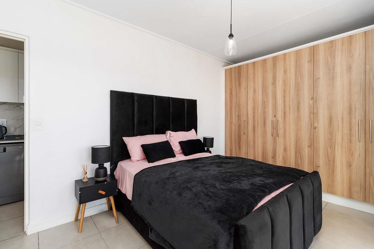 A well-maintained bedroom featuring modern built-in wooden cupboards, neutral tiled flooring, and a contemporary pendant light fixture.