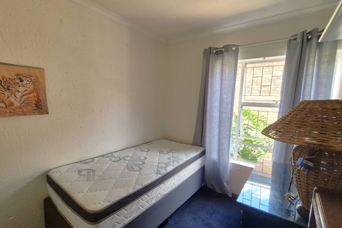 A compact bedroom featuring a window with security bars and neutral wall finishes.