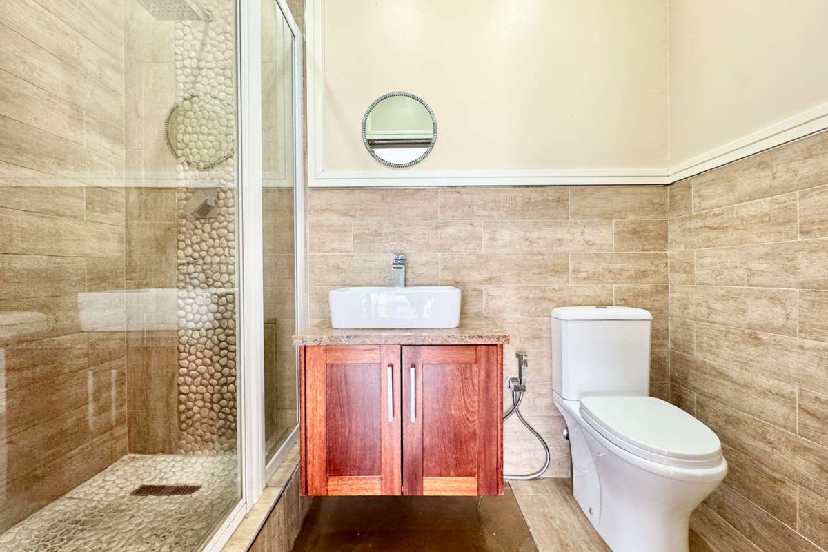 A modern bathroom featuring a glass-enclosed shower with pebble tile accents, a floating wooden vanity with a vessel sink, and a white toilet.