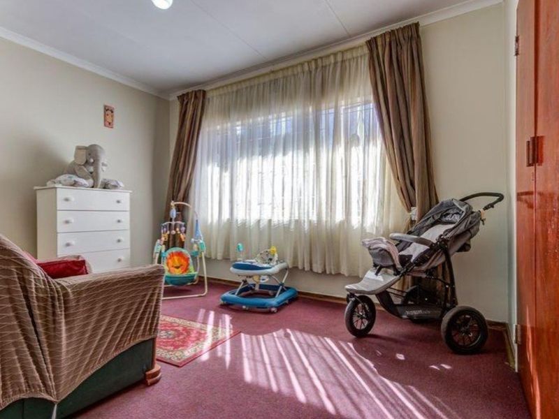 A bedroom featuring carpeted flooring, a large window with curtain rails, and a built-in cupboard.