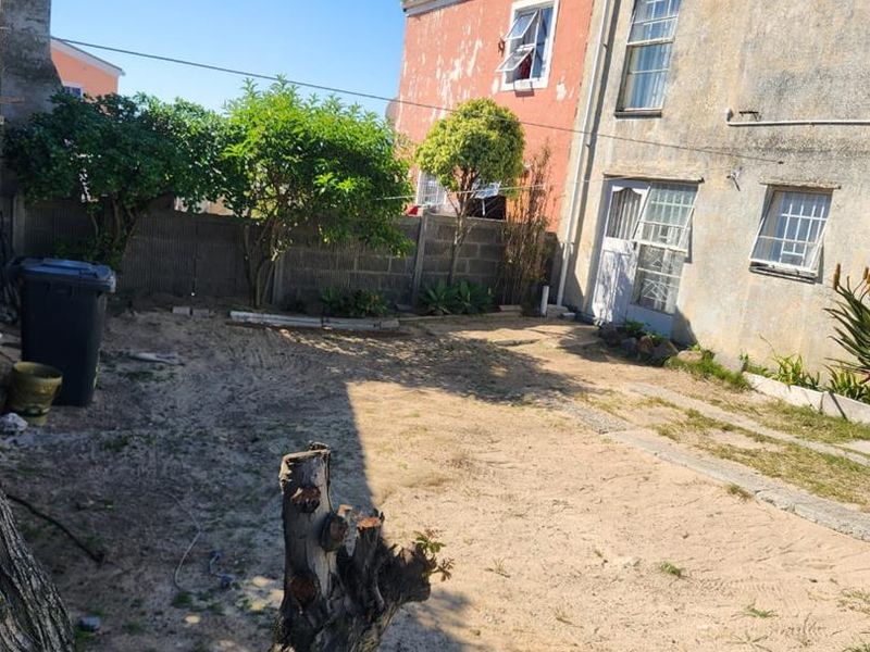 Rear exterior view of the property featuring a large unlandscaped garden area and a building facade showing significant signs of wear and weathering.