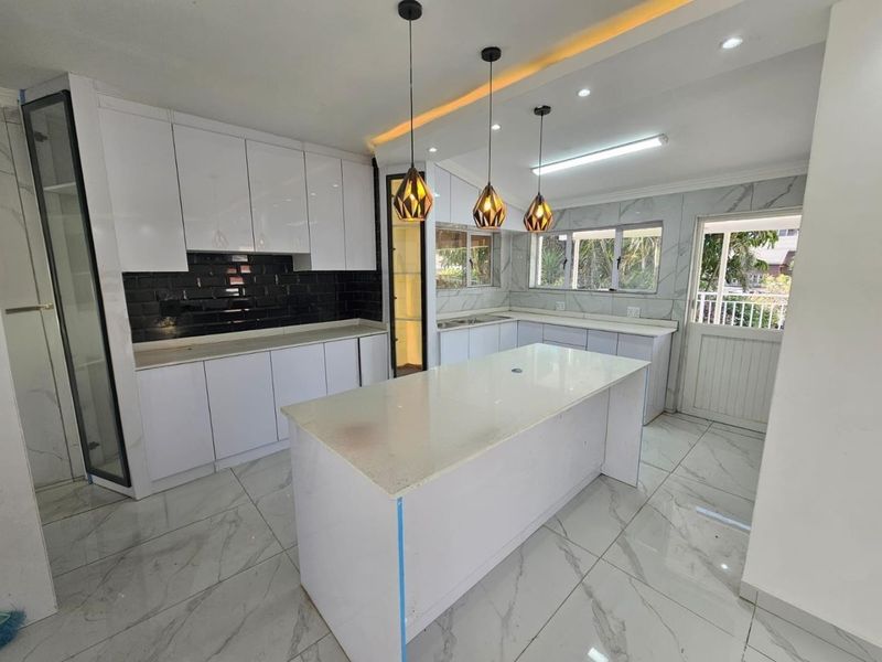 Modern kitchen featuring a central island, white cabinetry, quartz countertops, black subway tile backsplash, and marble-look floor tiles with recessed and pendant lighting.