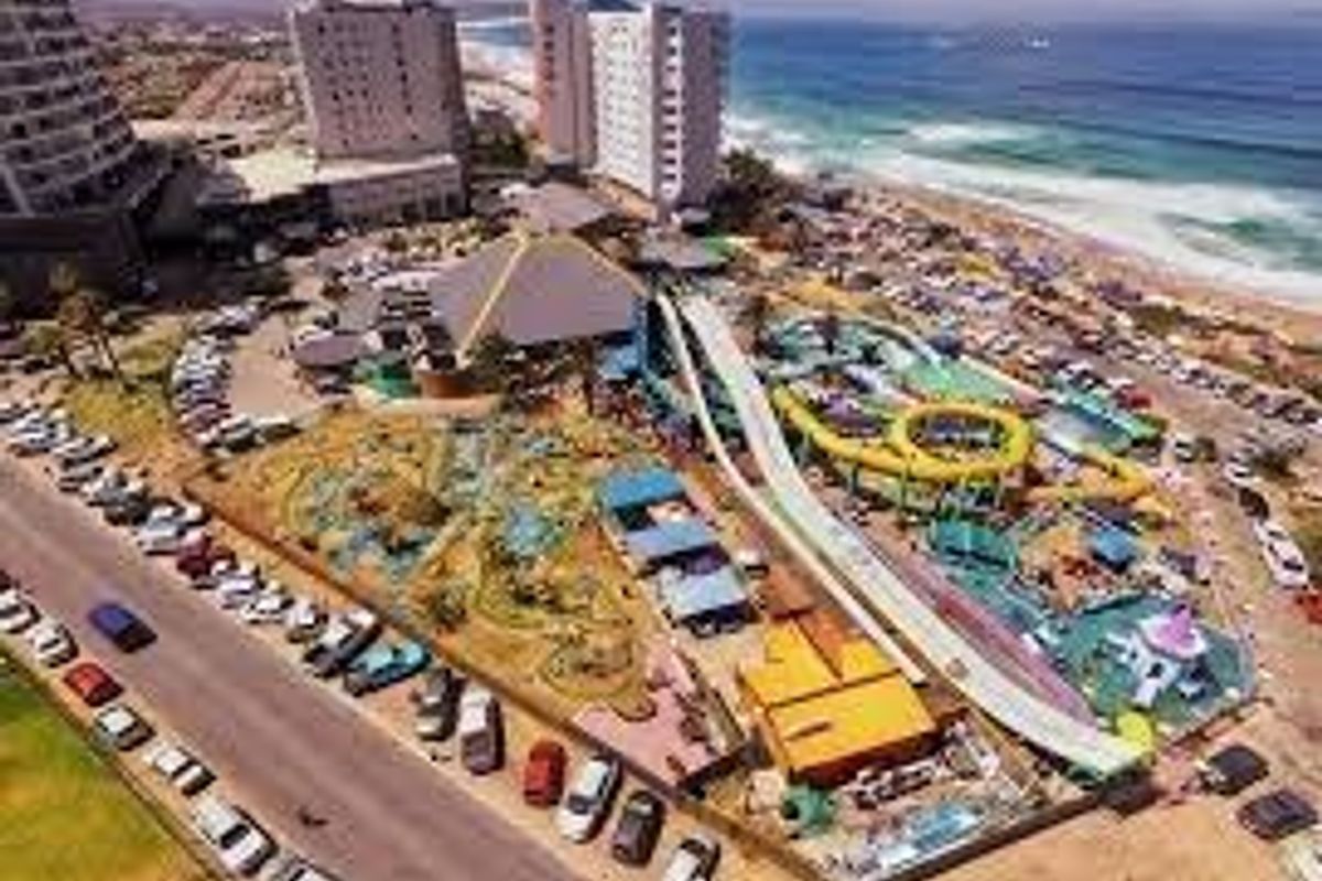 Aerial view of a coastal recreational facility featuring water slides, pools, and surrounding parking areas near the beach.