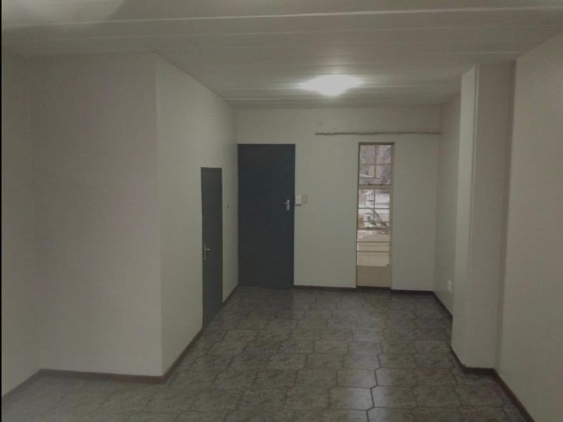 An empty, neutrally painted living area featuring tiled flooring, internal doors, and a window with security bars.