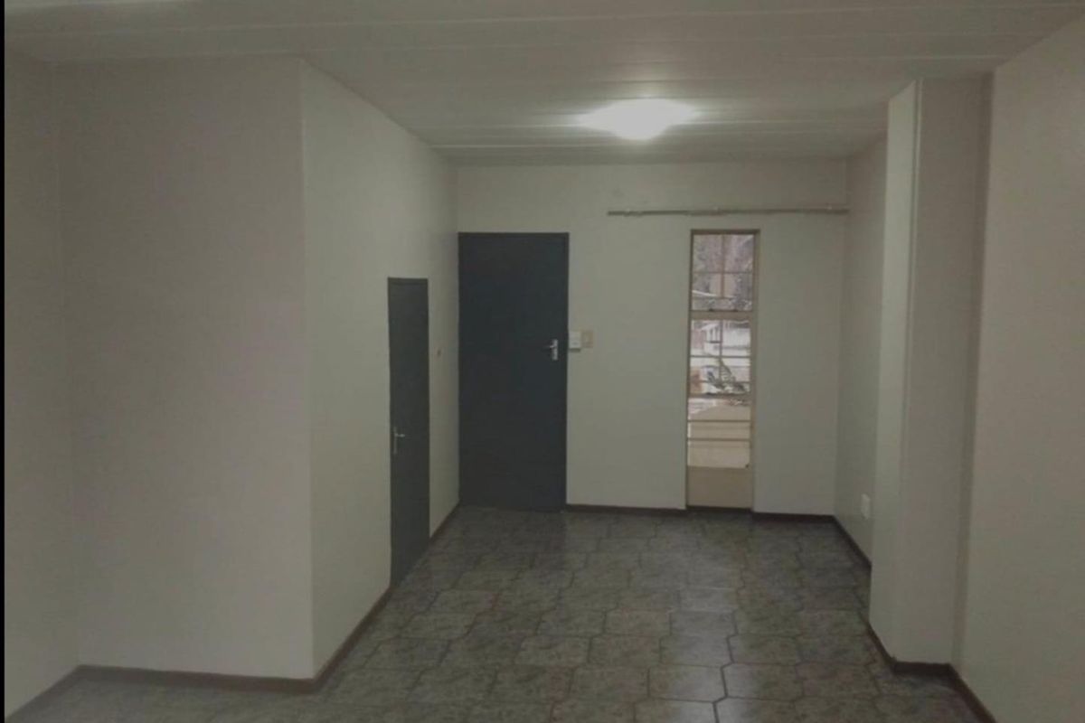 An empty, neutrally painted living area featuring tiled flooring, internal doors, and a window with security bars.