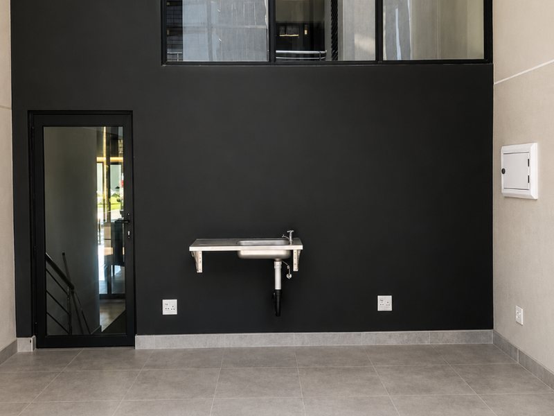 A clean, modern utility space featuring a wall-mounted stainless steel sink, large black-framed glass windows, and neutral floor tiling.