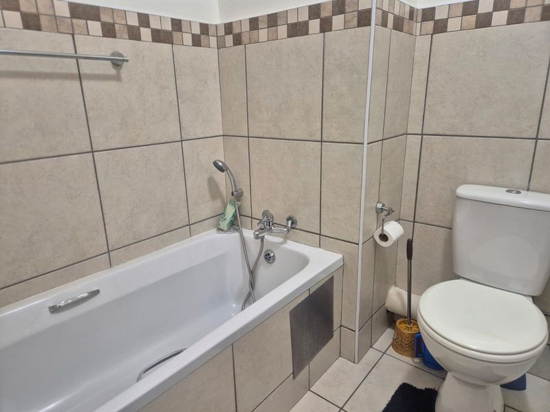 A functional bathroom featuring a bathtub with a handheld shower mixer, a standard toilet, and neutral-toned wall and floor tiling.