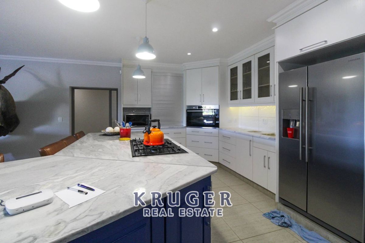 Modern kitchen featuring a large central island with stone countertops, built-in oven, gas hob, and ample white cabinetry with integrated appliance space.