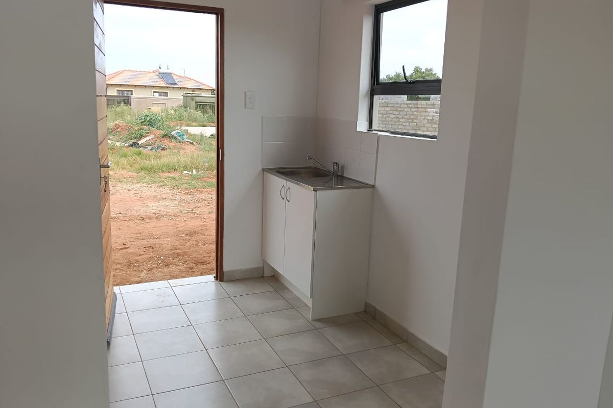 A compact kitchen area featuring a single sink unit, tiled flooring, and direct access to the exterior through a wooden door.