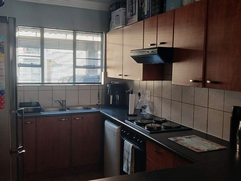 Functional kitchen featuring wooden cabinetry, dark laminate countertops, tiled splashbacks, and integrated cooking appliances with a window providing natural light.