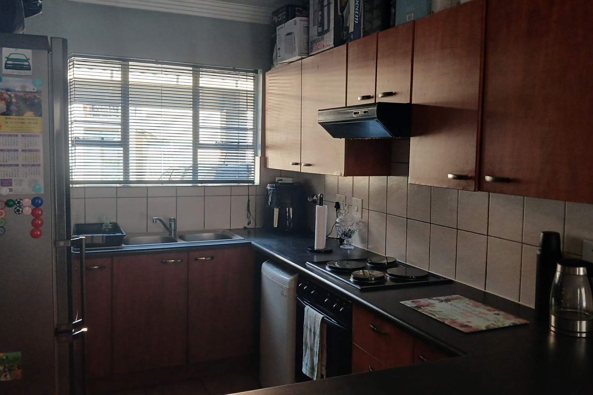 Functional kitchen featuring wooden cabinetry, dark laminate countertops, tiled splashbacks, and integrated cooking appliances with a window providing natural light.