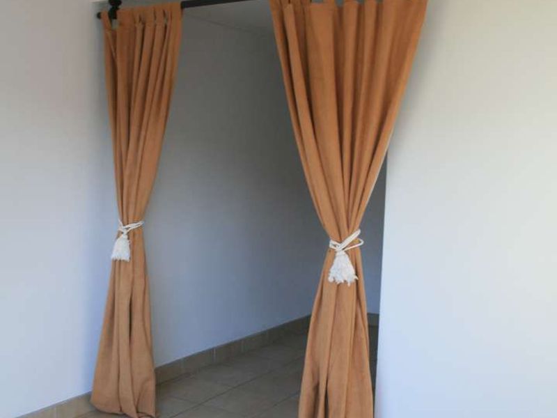 An empty room featuring neutral tiled flooring and a simple ceiling light fixture, currently partitioned by decorative fabric curtains.