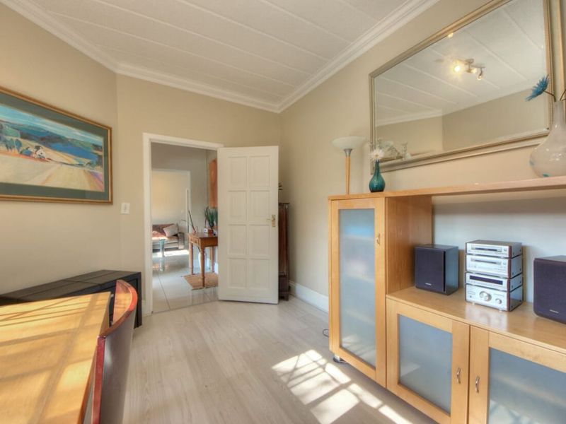 A well-maintained living area featuring light laminate flooring, crown molding, and a classic panelled door leading to an adjacent room.