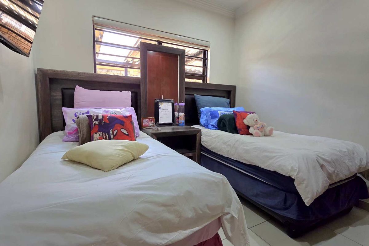 A bedroom featuring tiled flooring and a window with security bars, providing a functional space for rest.