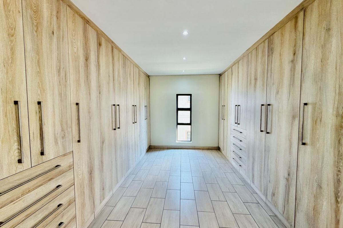 A spacious walk-in dressing room featuring extensive floor-to-ceiling built-in cabinetry with a light wood finish and modern tiled flooring.