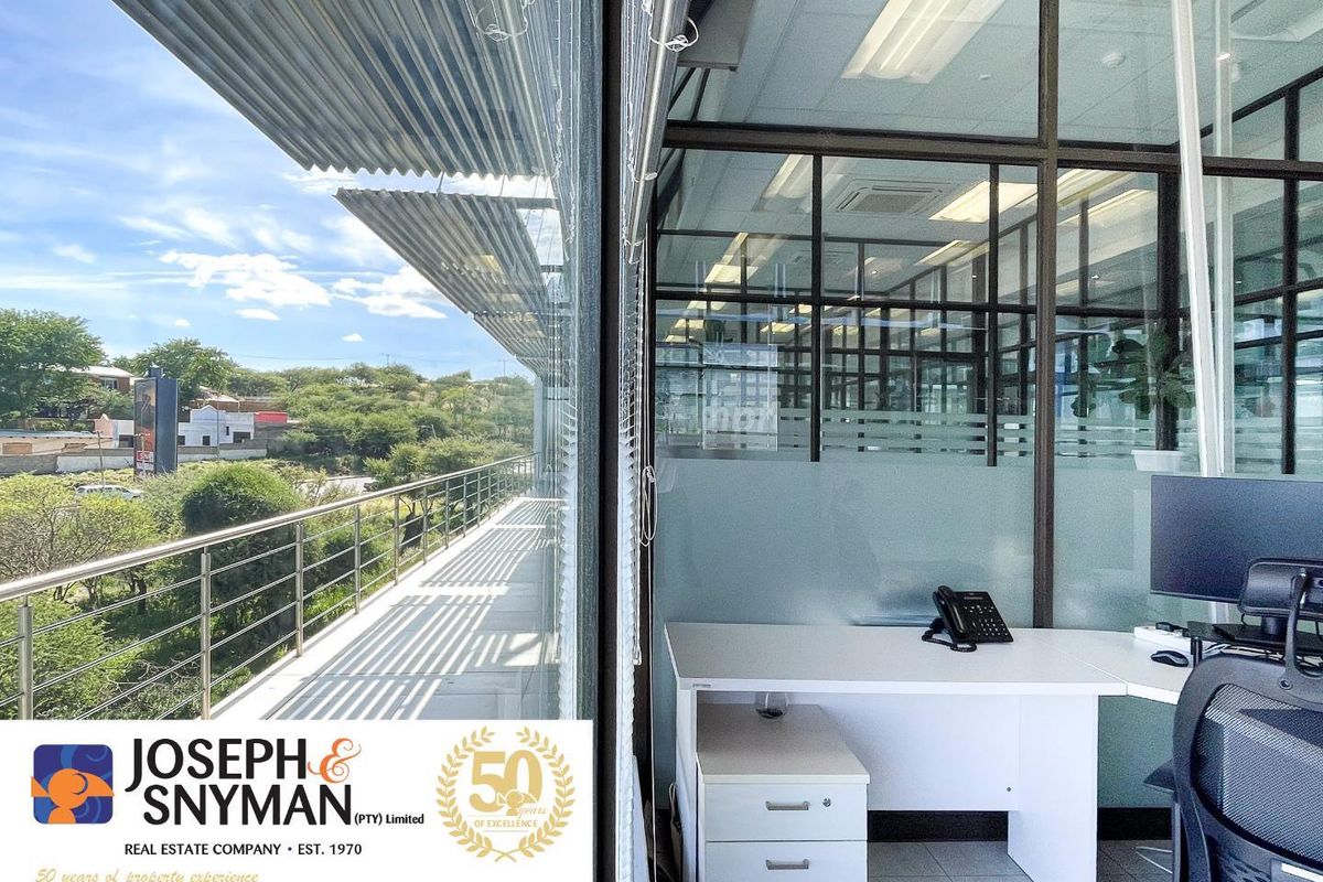 Modern office space featuring floor-to-ceiling glass partitions, tiled flooring, and direct access to a private balcony with scenic views.