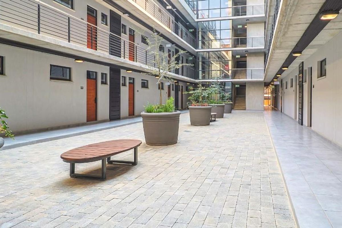 A modern, open-air apartment complex courtyard featuring paved walkways, multi-level access balconies, and contemporary architectural design.
