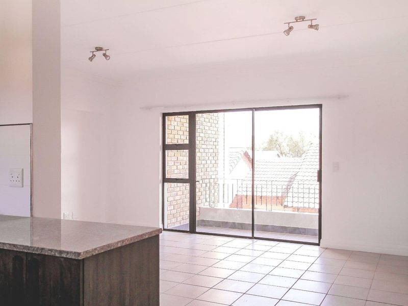 Spacious open-plan living area featuring tiled flooring, modern spotlighting, and a kitchen island with granite countertop, leading out to a private balcony.