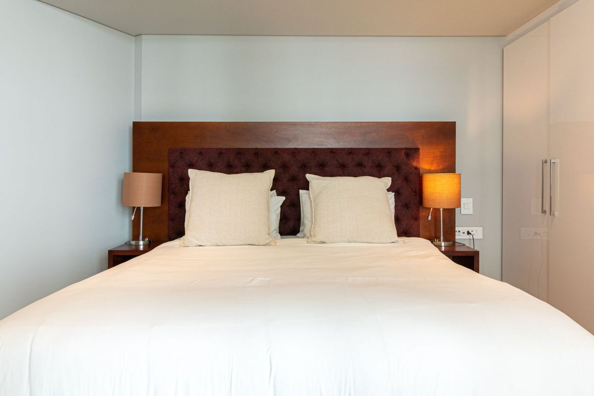 A well-maintained bedroom featuring a built-in wardrobe and a custom upholstered headboard with integrated bedside lighting.