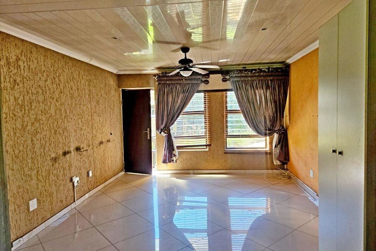 A spacious bedroom featuring tiled flooring, a ceiling fan, and built-in wardrobe storage, offering a blank canvas for potential interior updates and modernization.