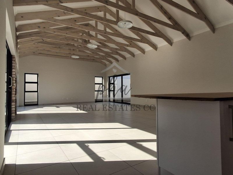 Spacious open-plan living area featuring high vaulted ceilings with exposed timber trusses, tiled flooring, and a modern kitchen island with sink.
