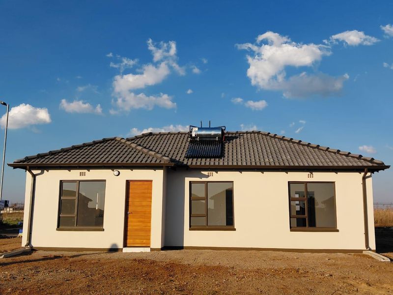 A modern single-story house exterior featuring a tiled roof, solar water heating system, and aluminium-framed windows with a timber front door.