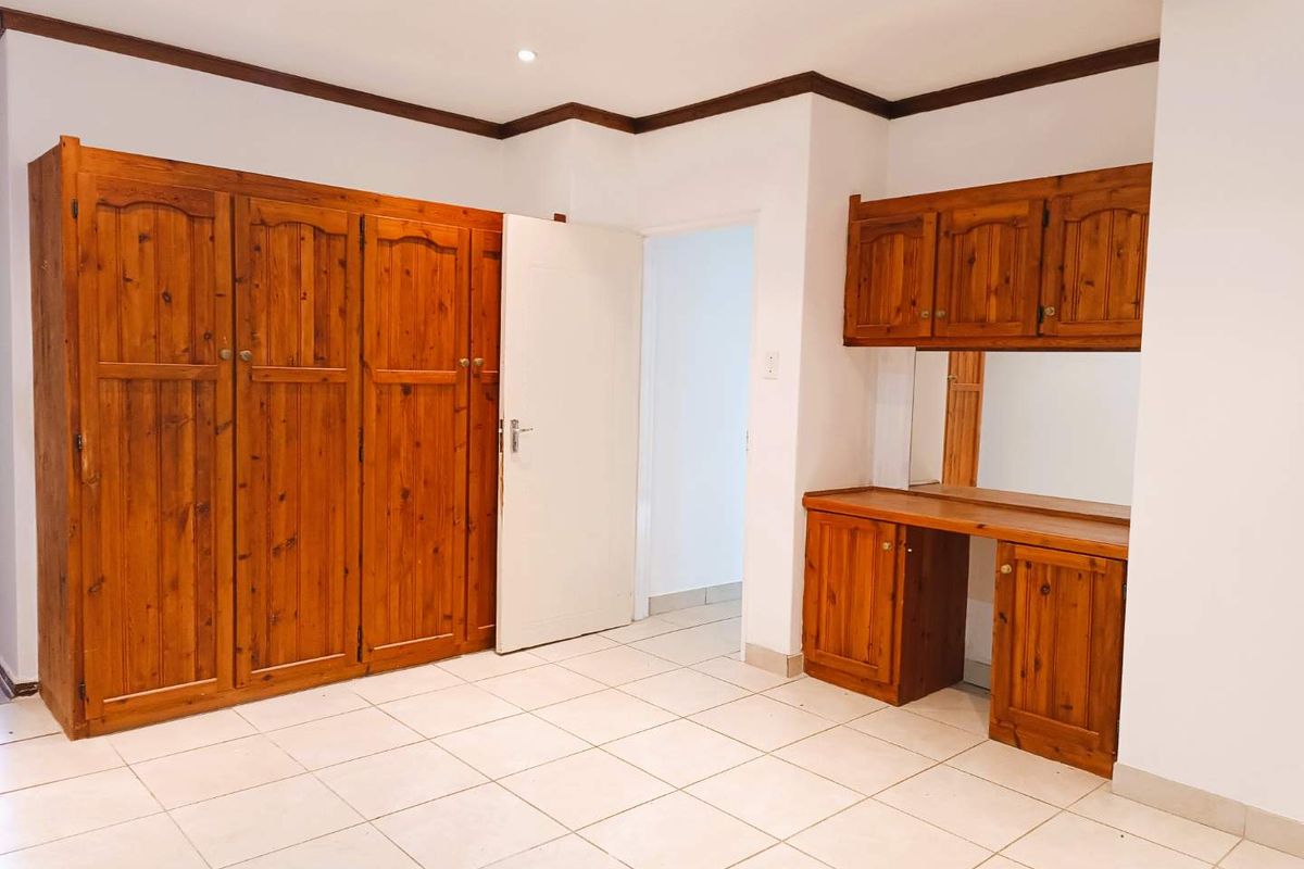 A bedroom featuring built-in wooden wardrobes and a matching vanity unit with tiled flooring and recessed ceiling lighting.