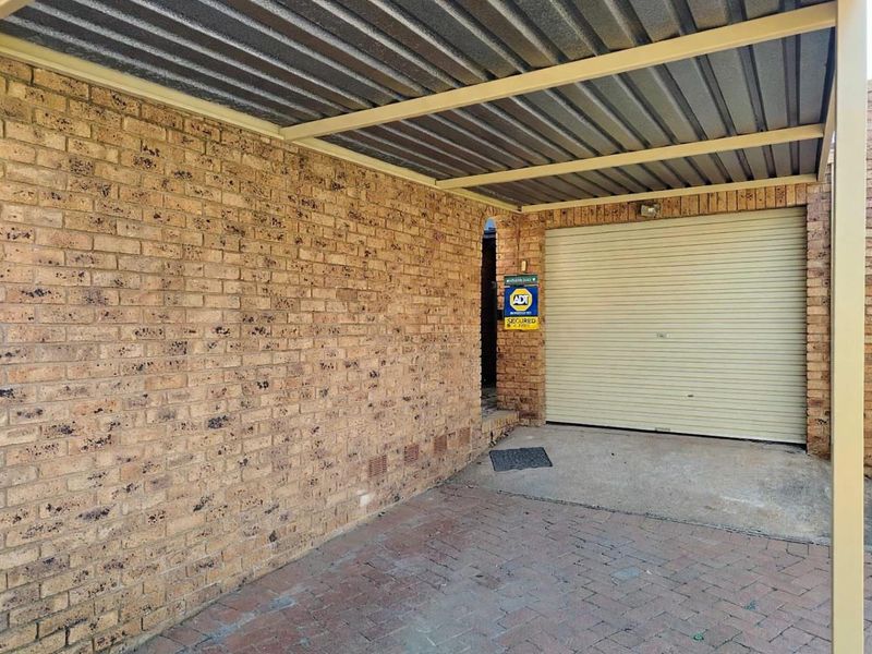 A covered carport area featuring a brick facade and a secure roller garage door entrance.