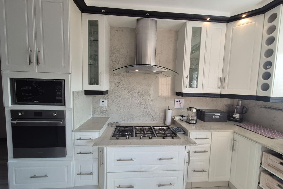 A well-maintained kitchen featuring white shaker-style cabinetry, stone countertops, a built-in oven and microwave, and a stainless steel gas hob with extractor fan.