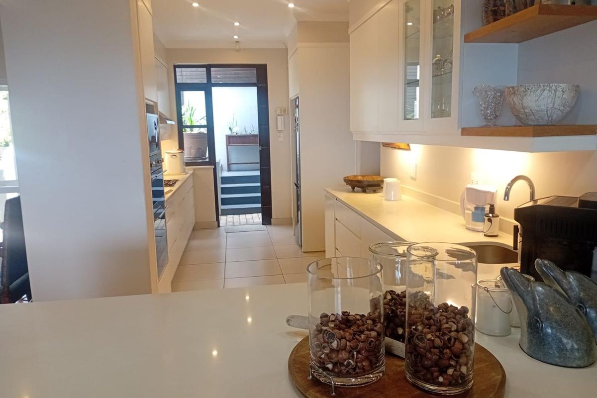 Modern kitchen featuring sleek white cabinetry, stone countertops, integrated appliances, and recessed lighting, leading to an outdoor staircase.