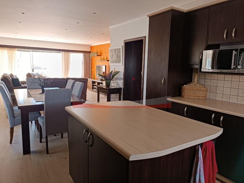 Open-plan living and dining area featuring a modern kitchen with dark cabinetry, laminate countertops, and integrated appliances, flowing into a spacious lounge.