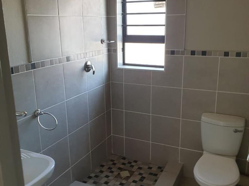 A functional bathroom featuring a walk-in shower, toilet, and basin with neutral wall and floor tiling.