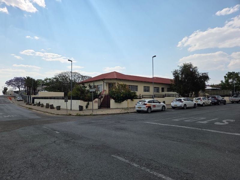 Street-level view of the office property featuring a perimeter wall, metal fencing, and a tiled roof structure.