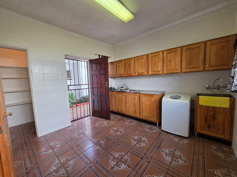 Functional laundry room featuring wooden cabinetry, tiled flooring, a stainless steel sink, and direct access to an outdoor area via a security gate.