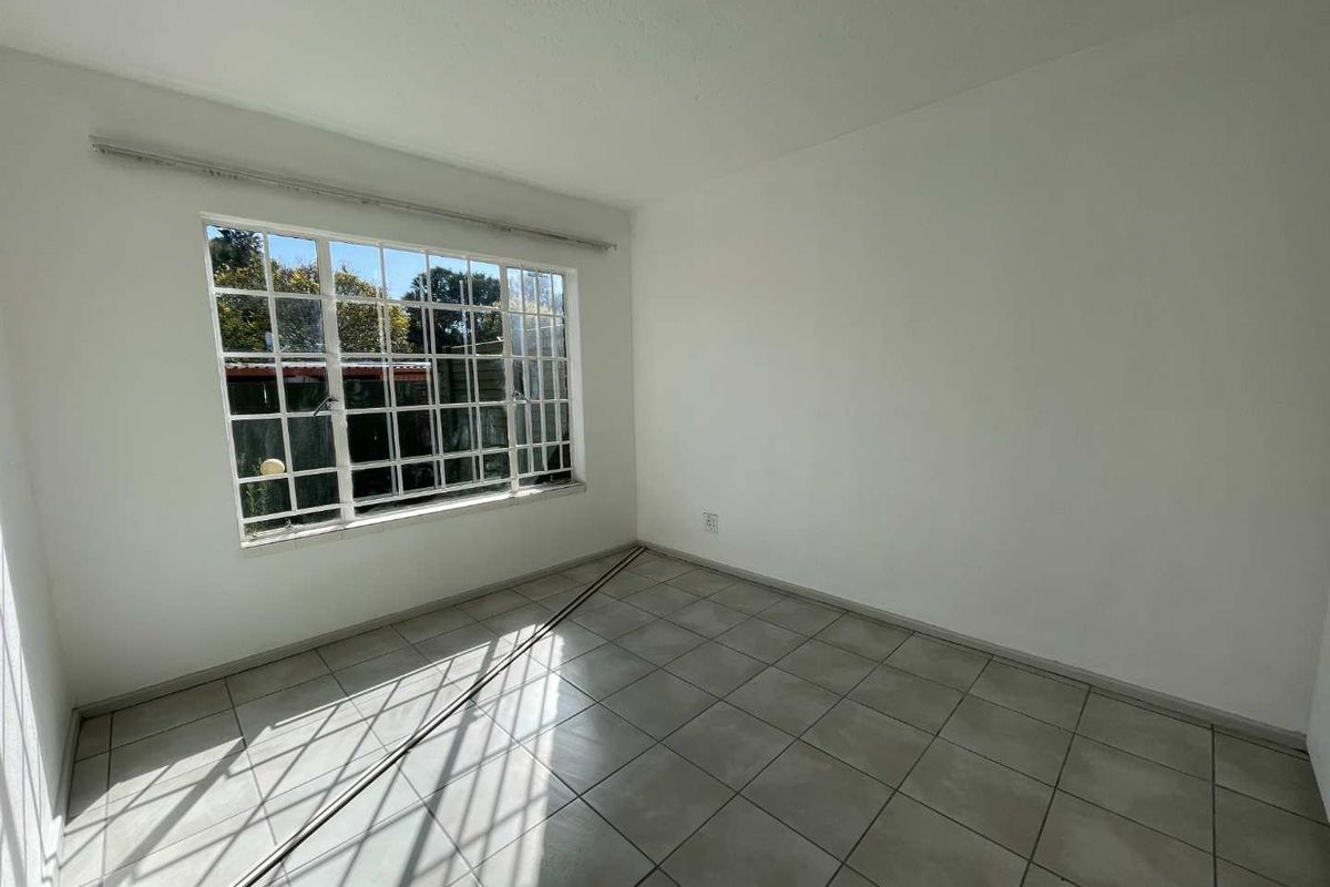An empty bedroom featuring neutral ceramic floor tiles and a large grid-pattern window allowing natural light.