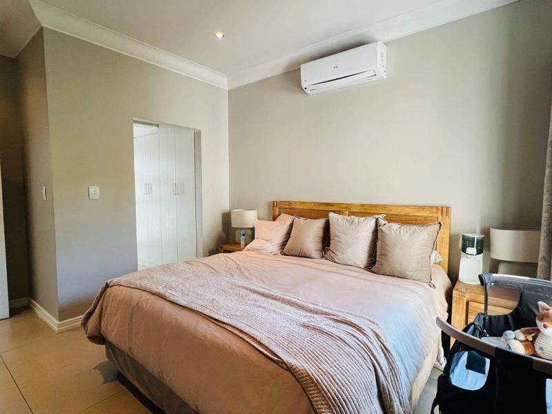 A well-maintained bedroom featuring tiled floors, built-in cupboards, and a wall-mounted air conditioning unit with access to an outdoor area via sliding doors.