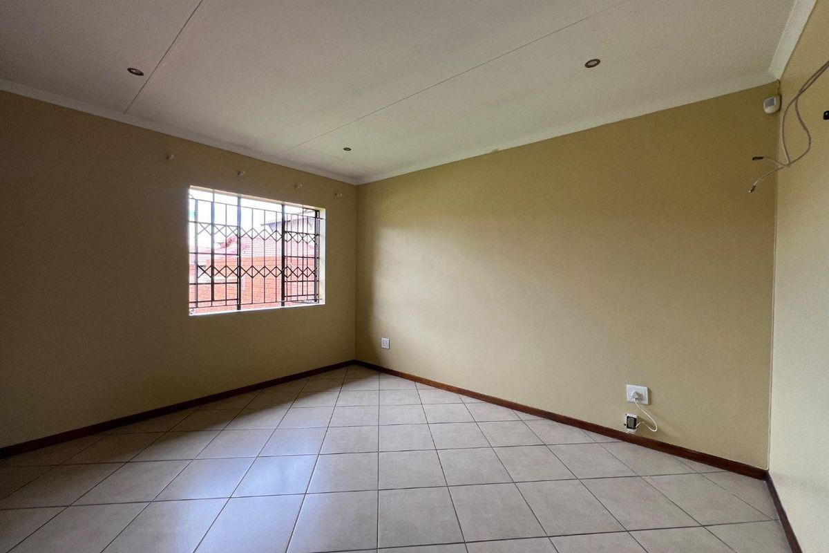An empty bedroom featuring tiled flooring, recessed downlights, and security bars on the window, providing a blank canvas for personalization.