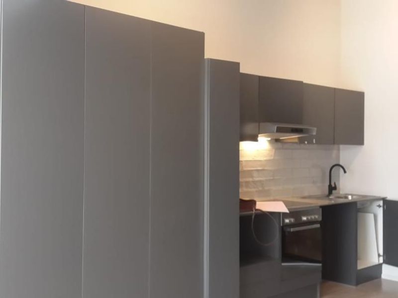 Modern kitchen featuring dark grey cabinetry, built-in oven and hob, tiled backsplash, and a striking exposed brick feature wall.