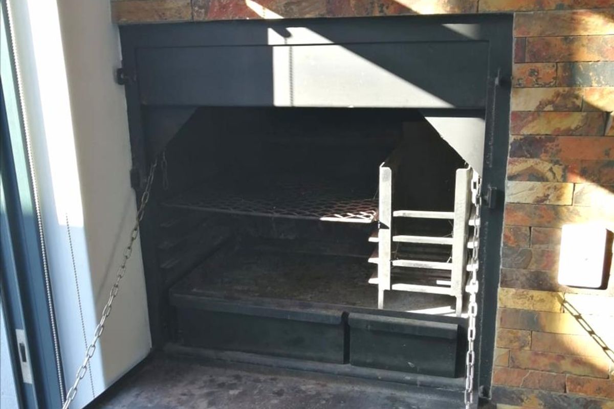 Built-in indoor braai unit featuring a stone-clad surround and integrated metal firebox with adjustable grill and coal maker.
