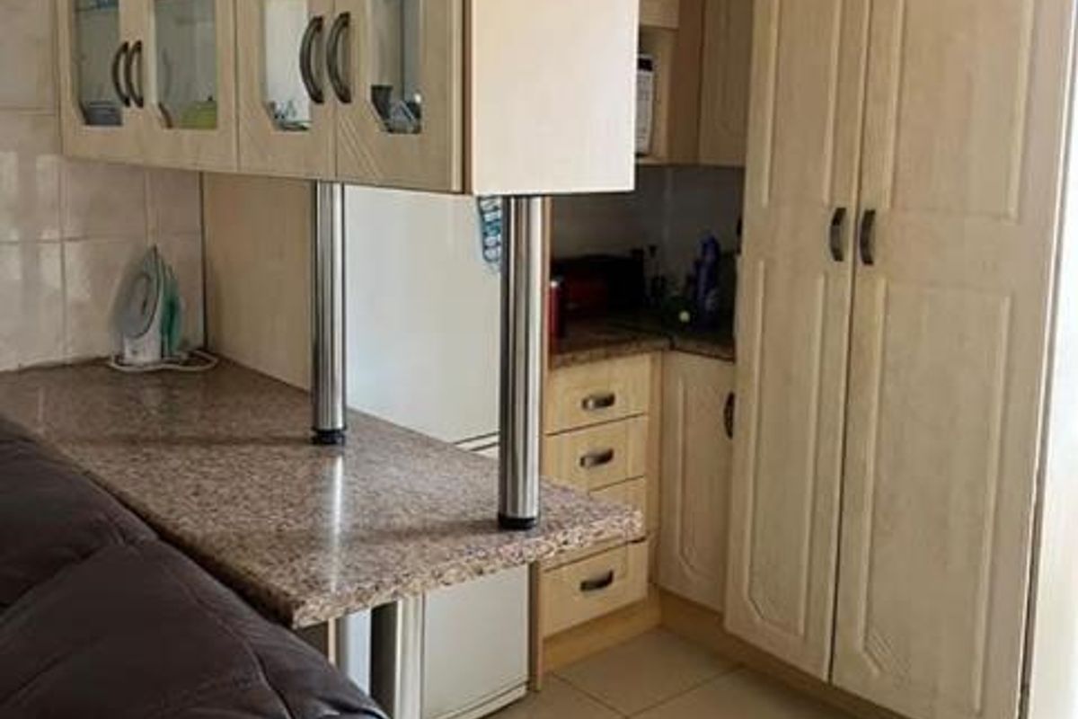 A compact kitchen area featuring light-toned cabinetry, granite-look laminate countertops, and tiled flooring, providing functional storage and prep space.