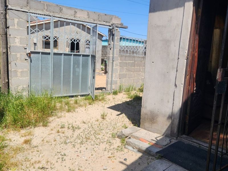 Rear exterior area featuring a concrete block boundary wall, metal security gate, and basic concrete paving leading to the building entrance.