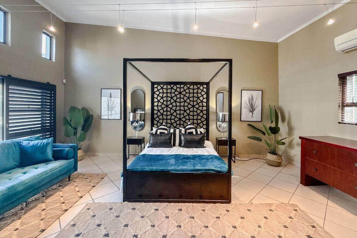 Spacious bedroom featuring high ceilings, tiled flooring, track lighting, and a wall-mounted air conditioning unit.