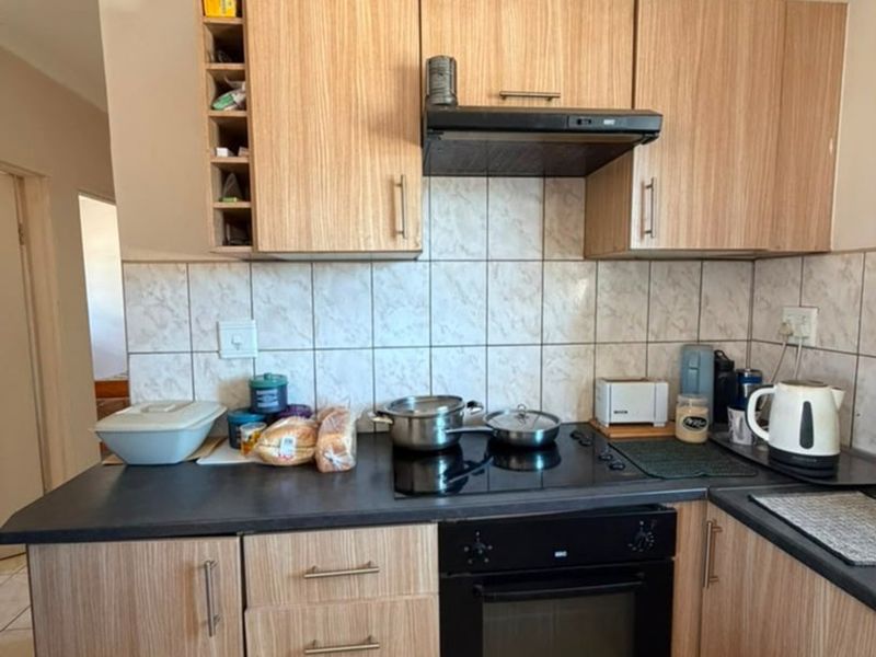 A functional kitchen featuring wood-look cabinetry, dark countertops, a tiled backsplash, and integrated cooking appliances including an oven and hob.