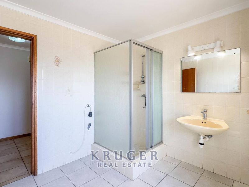 A functional bathroom featuring a shower enclosure, wall-mounted basin, and neutral tiled finishes throughout.