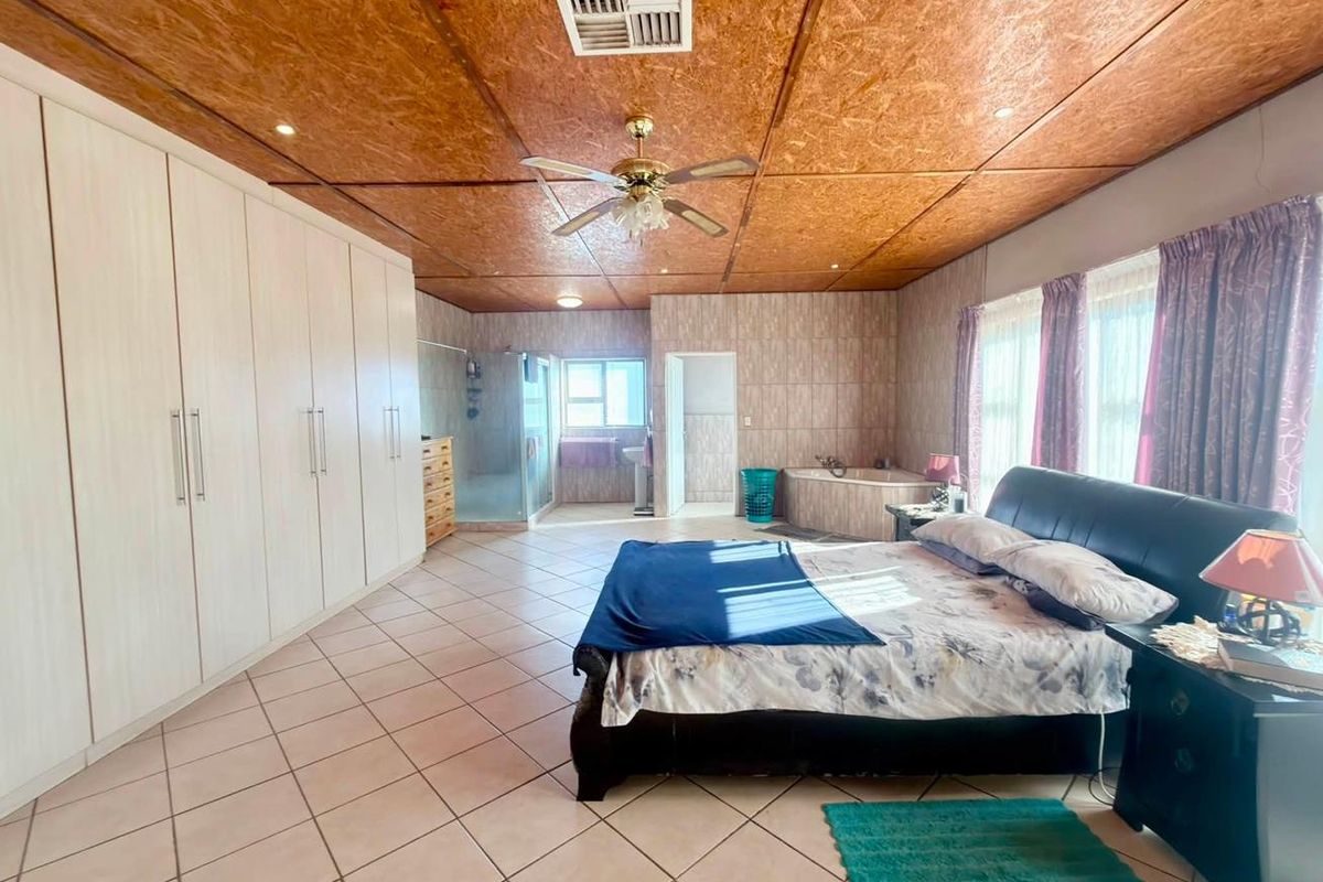 Spacious master bedroom featuring extensive built-in cabinetry, an open-plan en-suite bathroom with a corner tub and shower, and unique wood-textured ceiling panels.